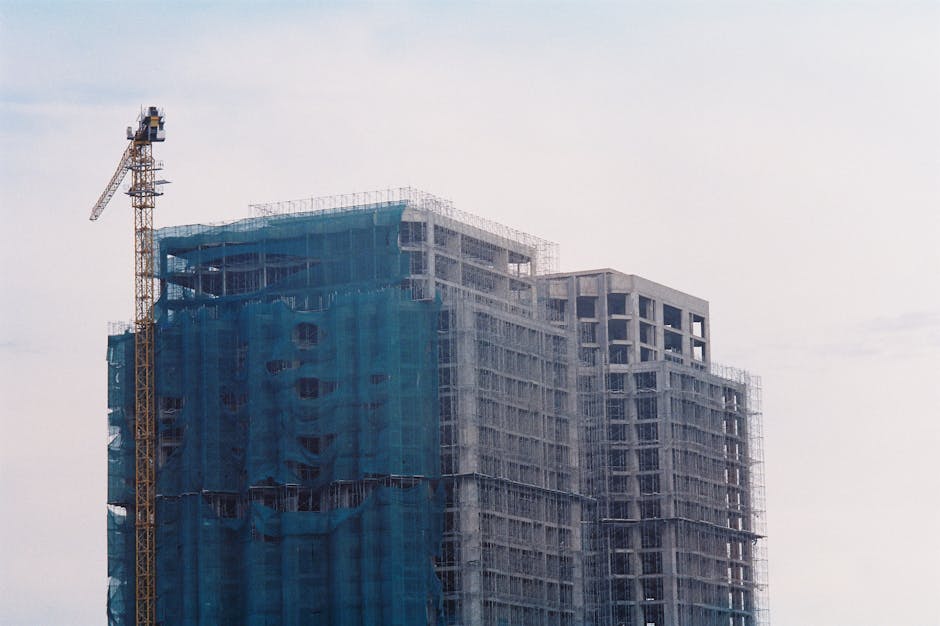 Construction site with cranes against cloudy sky, showing incomplete housing development