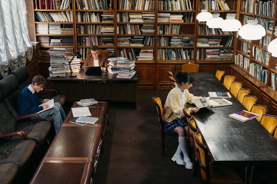 Young person reading intently by themselves at a library table surrounded by stacked books, warm lamp light, focused and self-directed energy