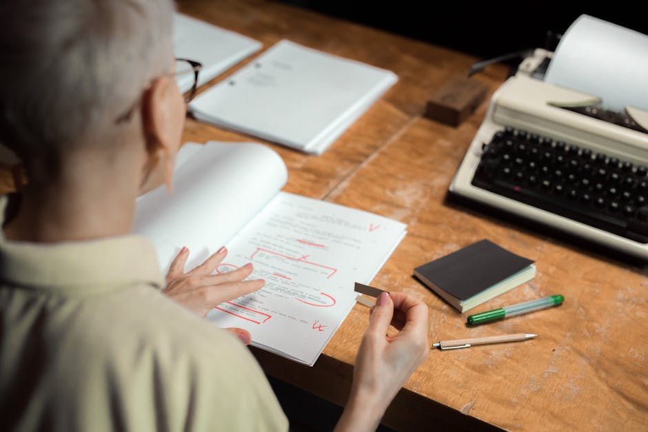 Two people sitting across from each other at a coffee shop, one reading a printed manuscript and marking it with a red pen, warm candid photography style