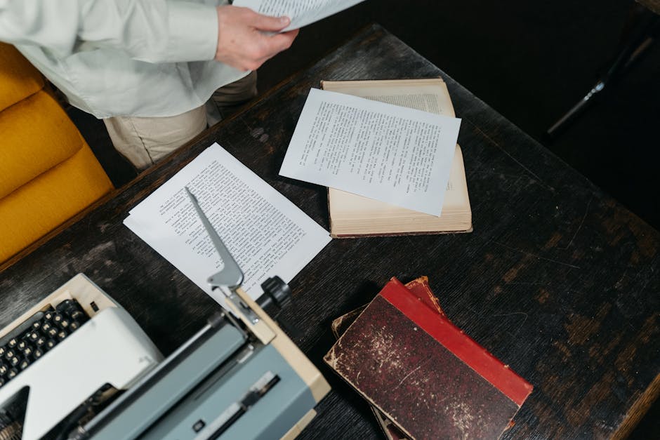 A writer at a wooden desk with warm lamplight, surrounded by printed manuscripts and an open laptop showing book analytics dashboards