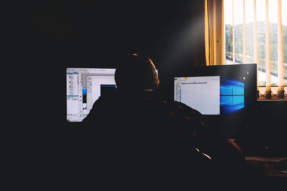 Person at a desk, dual monitor setup, one screen showing a terminal and one showing a desktop environment, focused and calm, warm ambient lighting