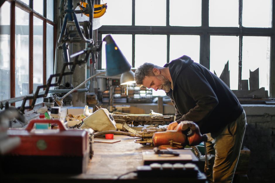 Person at a workbench using tools with focused concentration, natural workshop lighting, hands-on craftsmanship, warm tones, photorealistic