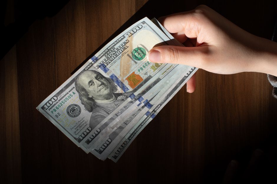 A crumbling dollar bill being held by worn working hands, dramatic chiaroscuro lighting, symbolic and cinematic, 8k detail