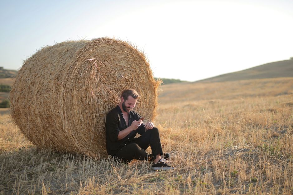 A person holding a smartphone showing a Bitcoin wallet in an open field — wide sky, sunlight, sense of autonomy and open space