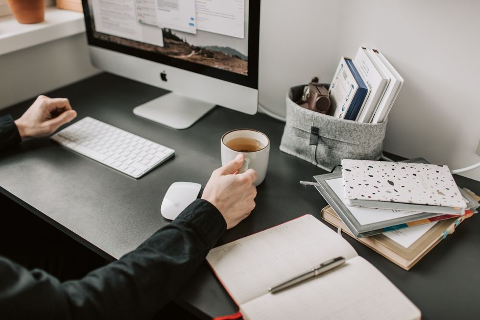 A person working focused at a well-organized home desk, natural window light, coffee cup, notebook beside laptop, calm productive atmosphere